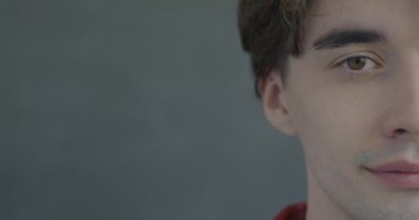 Siyah arka planda kameraya bakarak gülümseyen neşeli genç bir adamın yavaş çekim portresi. İnsanlar ve duygu kavramı.