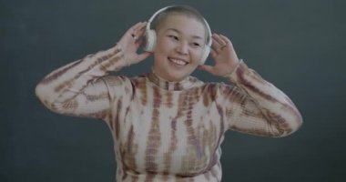 Kulaklıkla müzik dinleyen, siyah arka planda dans eden Asyalı genç bir kadının yavaş çekim portresi. İnsanlar ve eğlence konsepti.