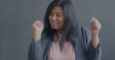 Yavaş çekimde dans eden, gülümseyen, hareketli ellerle siyah arka planda kameraya bakan mutlu genç bir kadının portresi. İnsanlar ve eğlence konsepti.