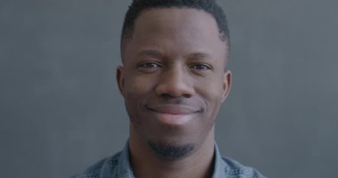 Siyah arka plandaki kameraya gülümseyen Afrikalı Amerikalı adamın yavaş çekim portresi. İnsanlar ve olumlu duygu kavramı.