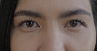 Asyalı kadın gözlerinin, duygusuzca yanıp sönen kameraya bakışının yavaş çekim portresi. İnsanlar ve insan vücudu ayrımı kavramı.