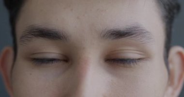 Gri arkaplanda duygusuz bir şekilde kameraya bakan Asyalı genç erkeklerin yavaş çekim portresi. İnsanlar ve yüz ifadesi kavramı.