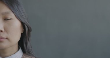 Siyah arka planda duygusuz bir şekilde kameraya bakan Asyalı genç bir kadının yakın plan portresi. İnsanlar ve ifade kavramı.
