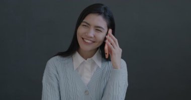 Cep telefonuyla konuşan neşeli Asyalı genç bir kadının portresi siyah arka planda gülüyor. İnsanlar ve cep telefonu iletişim kavramı.