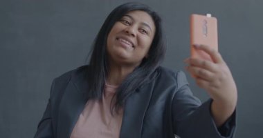 Siyah arka planda akıllı telefon kamerası için selfie çeken güzel bir genç kızın yavaş çekim portresi. Fotoğraf ve modern teknoloji kavramı.