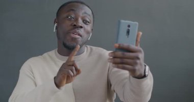 Afro-Amerikalı bir adam internet üzerinden telefon ve kulaklıkla konuşuyor. Gri arkaplanda jestler yapıyor. İnsanlar ve iletişim konsepti.