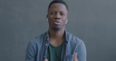 Siyah arkaplanda kablosuz kulaklık kullanarak kameraya bakarak online video konuşması yapan Afrikalı Amerikalı adamın portresi.