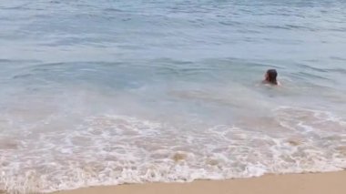 Yakışıklı, uzun saçlı genç sıcak bir yaz gününde denizde yüzer. Dostane yaz konsepti, sağlıklı yaşam tarzı konsepti, yaz tatili.