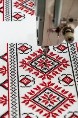 Makine çapraz dikiş. Tuvaldeki kırmızı ve siyah ipliklerle çapraz dikiş. Dikiş makinesine çapraz dikiş, yakın çekim, seçici odaklanma. Ukrayna acelesi, folklor desenli süs
