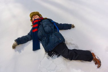 Karda yatan tatlı çocuk. Kışın bir çocuk dışarıda oynuyor. Manzaralı. Kış eğlencesi dışarıda, kış tatili. Aile zamanı.