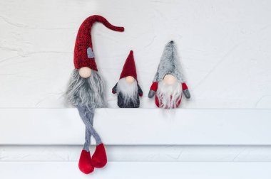Elfler, Noel süsleri. Üç cüce, duvarın karşısındaki beyaz ahşap bir rafta oturuyor. Noel ve Yeni Yıl konsepti, tebrik kartı, kopyalama alanı