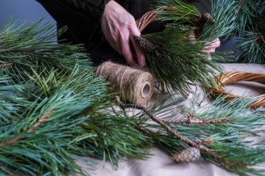 Kırsal Noel çelengi yapıyorum. Çam ağacı dalları, koniler, ışıklar olan ahşap masanın arka planındaki kadın elleri. Tatil hazırlıkları.