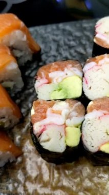 Suşi ruloları. Siyah tabakta çeşit çeşit suşi var. Çubukları kullanarak siyah tahta tahtadan bir suşi rulosu al ve yaklaş. Japon yemekleri yeme konsepti
