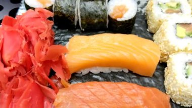 Suşi ruloları. Siyah tabakta çeşit çeşit suşi var. Çubukları kullanarak siyah tahta tahtadan bir suşi rulosu al ve yaklaş. Japon yemekleri yeme konsepti