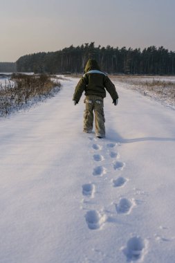 Küçük çocuk doğada yürüyor. Karda ayak izleri. Sağlıklı aktif yaşam