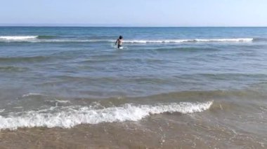 Uzun saçlı ve siyah mayosu olan çocuk yazın açık denizde yürüyor.. 