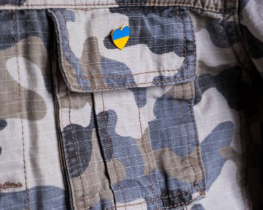 Metal badge with the flag of Ukraine in the shape of a heart on military jacket. Support for Ukraine. War in Ukraine. Ukraine flag theme