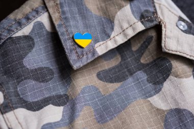 Metal badge with the flag of Ukraine in the shape of a heart on military jacket. Support for Ukraine. War in Ukraine. Ukraine flag theme