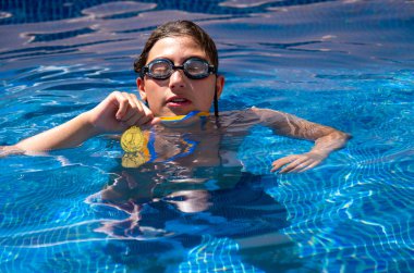 Successful caucasian young swimmer with award in outdoor pool. Golden trophy in swimming, teen boy showing off medal. Healthy lifestyle concept, sport activities