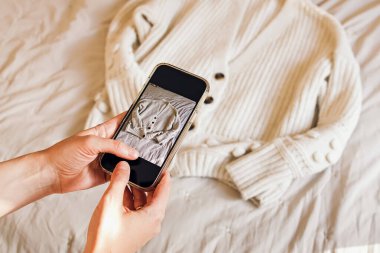 Giysilerinin fotoğrafını çeken kadınların ellerinin yakın çekimi. Kullanılmış giysilerin çevrimiçi satılması, yeniden kullanımı, sürdürülebilir tüketim