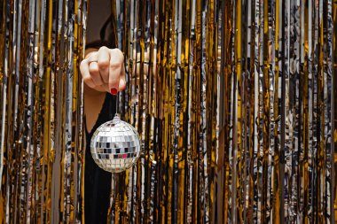 Parlak perdelerin arasında dekoratif disko topu tutan kadının eli.