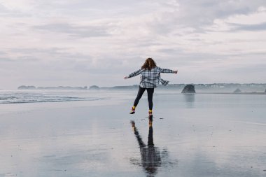 Oregon sahilinde, açık havadan hoşlanan bir kadın, sahilde bulutlu bir gün, suda yansıması olan bir kadın.