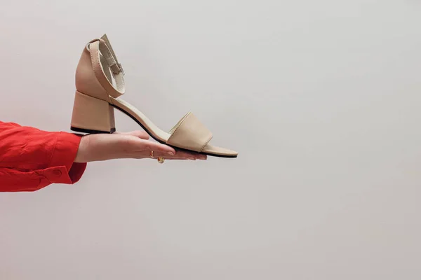 Vrouwelijke Hand Houden Beige Sandaal Tegen Witte Muur Stijlvolle Mode — Stockfoto