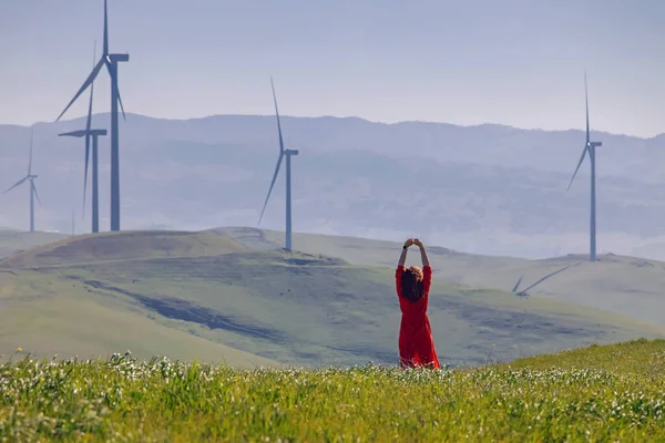 Woman enjoying clean air on the green meadow with wind turbines on the background. Clean air, green energy concept