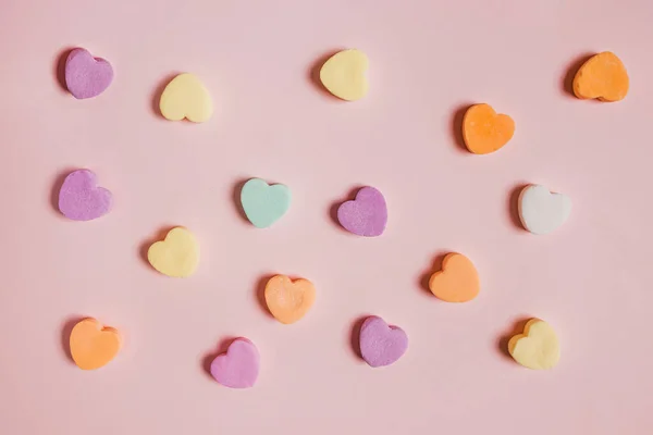 Colorful heart shaped candies on pastel pink background, Valentine\'s day backdrop