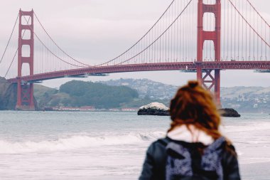 Woman looking on the Golden gate bridge, selective focus on the bridge, cloudy day in San Francisco, California