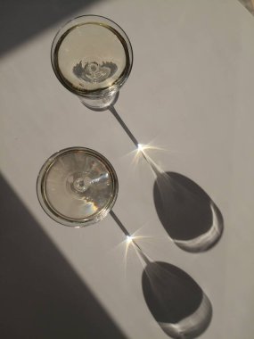 Two glasses of white wine on the white table in natural sunlight with long shadows