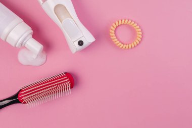 Brush, water spray bottle, curl styling mousse. Products for styling curly hair. Flat lay on pink background.