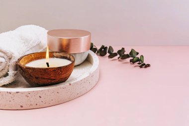 Still life body and face care items and candle in coconut shell on pink background