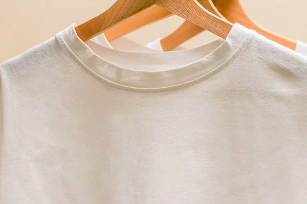 White cotton t-shirts on wooden hangers close-up