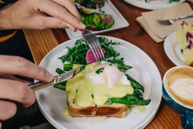 Erkek ellerinin yakın çekimi bıçakla kesilmesi haşlanmış yumurtayla kadeh kaldırılması, lezzetli bir brunch.