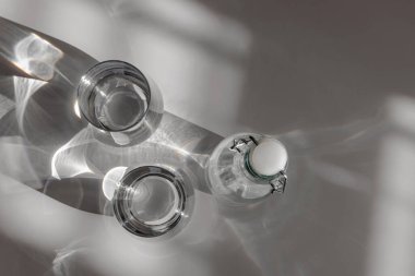 Cam şişe ve temiz suyla birlikte iki bardak uzun gölgeli, susuz ve sağlıklı bir yaşam tarzı olan doğal bir ışıkta.