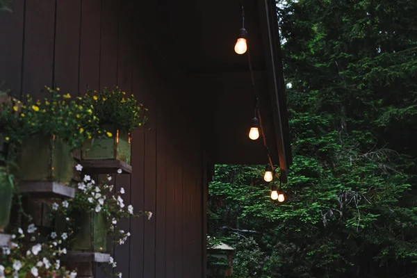 Cozy patio of wooden cabin decorated with warm light garland, summer night