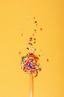 Parlak sarı arka planda plastik kaşığa renkli şeker serpintileri, diyette şeker, yaratıcı konsept