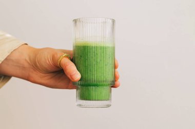 Beyaz duvarın üzerinden izole edilmiş taze yeşil smoothie bardağı tutan bir kadın eli. Sağlıklı yaşam tarzı.