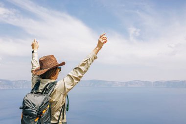 Şapkalı bir kadın elleri havada, göl manzaralı, yaz seyahati