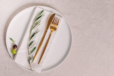 Altın renkli çatal bıçak takımı ve zeytin dalı, zarif masa ayarları, üst manzara.