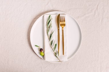 Altın renkli çatal bıçak takımı ve zeytin dalı, zarif masa ayarları, üst manzara.