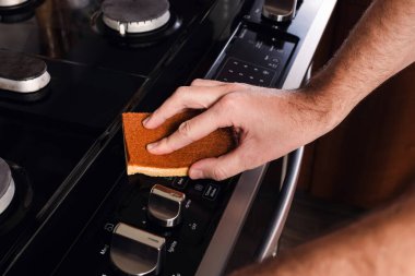 Mutfaktaki sobayı temizleyen adam, süngerle erkek elinin yakın plan görüntüsü.