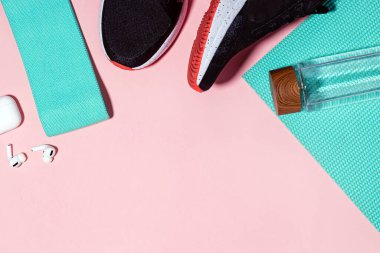 Ev aksesuarlarında spor ya da egzersiz. Spor ayakkabıları, paspas, pembe arka planda su şişesi..
