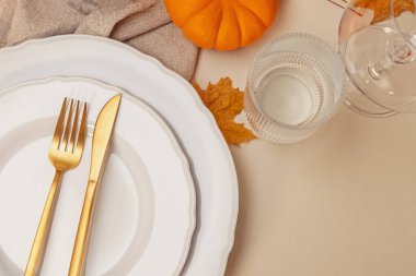 Şık bir sonbahar sofrası. Sonbahar yemeği için süslenmiş masa, beyaz tabaklar ve altın çatal bıçak, üst manzara.