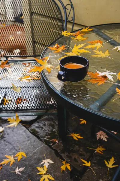 Cup of coffee standing on the patio table after the fall rain with lots of fallen yellow leaves