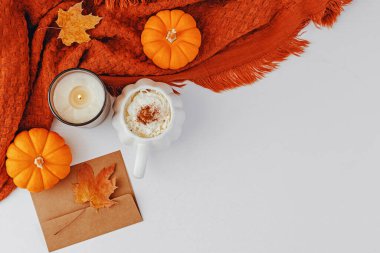 Balkabağı şeklindeki bardakta baharatlı latte, dekoratif küçük balkabakları ve ekoseli kahveyle sıcacık sonbahar kompozisyonu.