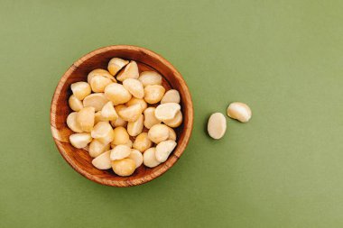 Yeşil arka planda küçük bir ahşap kasede Macadamia fındıkları.