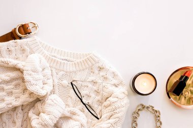 Konforlu sonbahar dairesi beyaz kablo örgü süveter, aksesuarlar, mum ve makyaj malzemelerinin yer aldığı yerde.