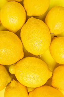 Close-up view of fresh lemons arranged on a vibrant yellow surface, summer background clipart